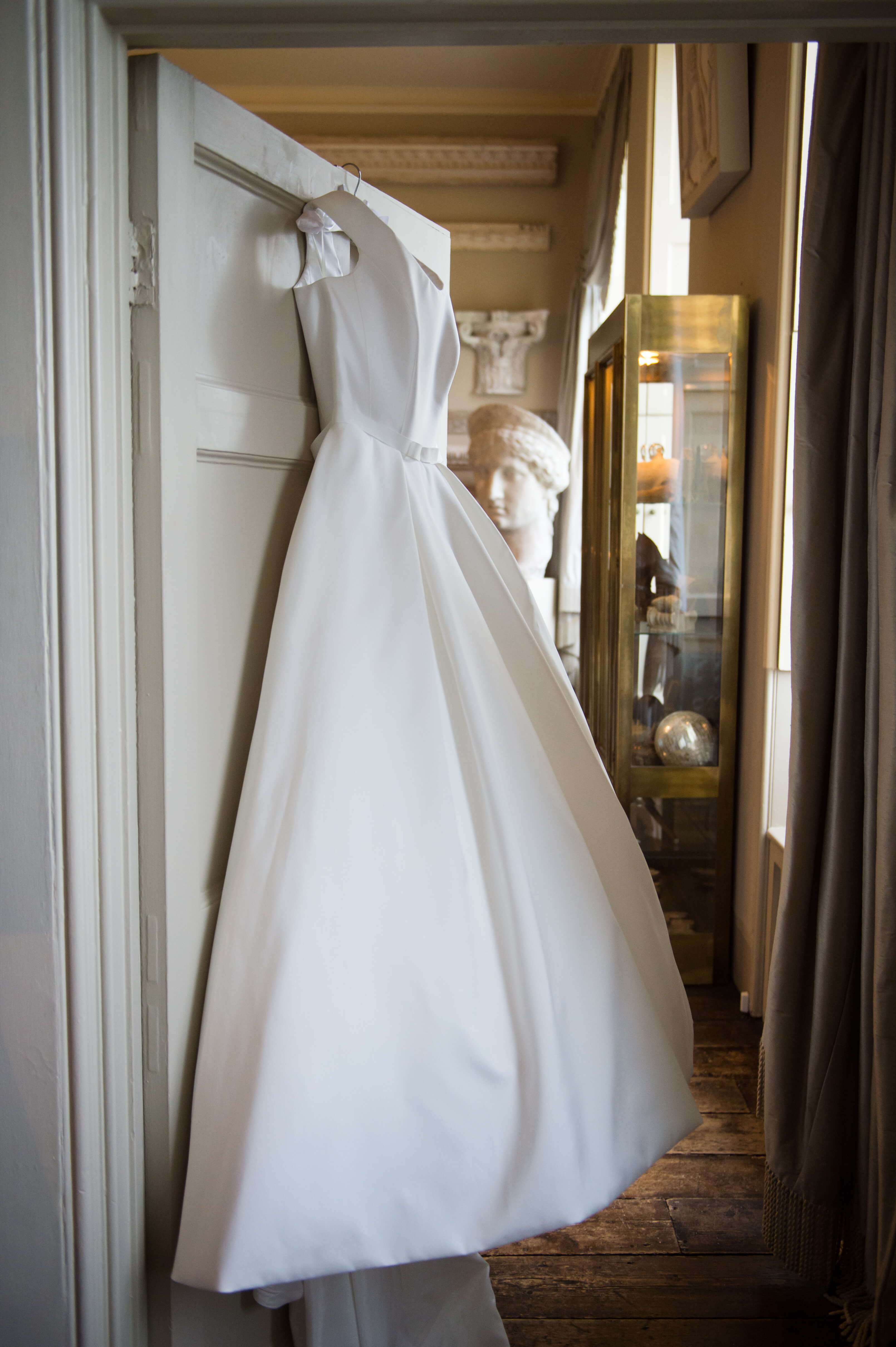 A beautiful white Suzanne Neville wedding gown hanging from a door at aynhoe park